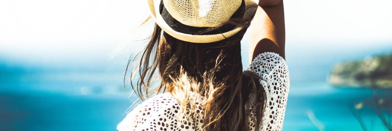 Tips for Eating Disorder Recovery in the Summer photo of a woman looking out at the sea in summer, wearing a hat