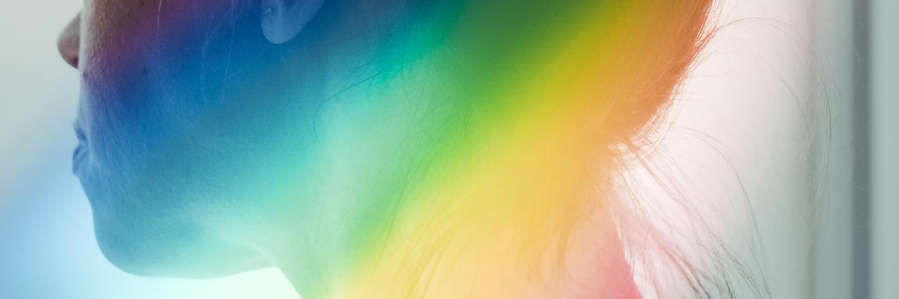 The Mental Health Impact of Being Forced to Come Out Before Ready photo of a woman looking out of a window with rainbow light flare
