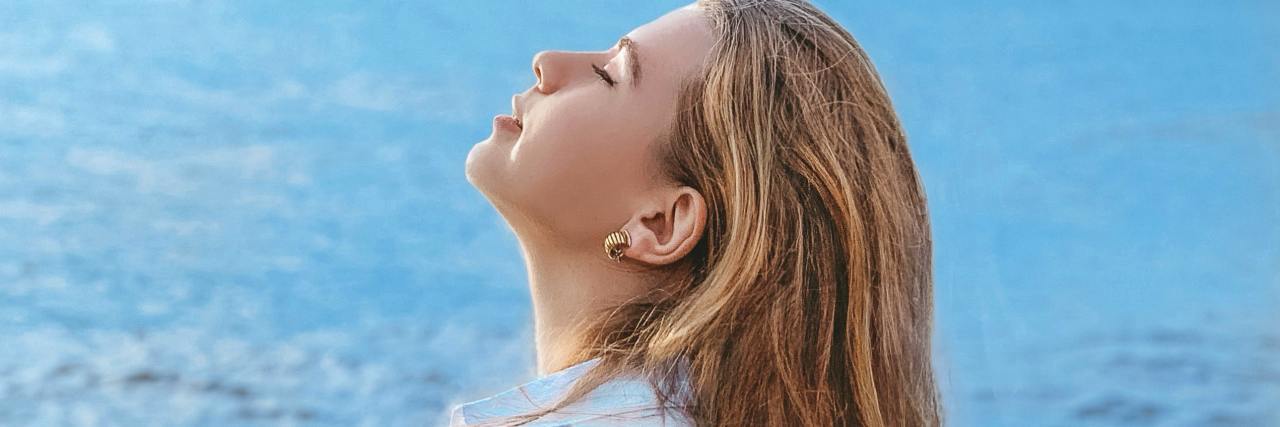 Finding Self-Acceptance on the Road to Self-Love With Bipolar Disorder photo of a woman raising her head and her eyes closed against an ocean background