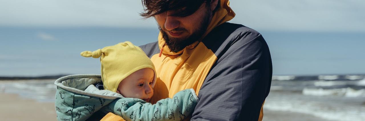 A man holding a baby at a beach, looking down at her