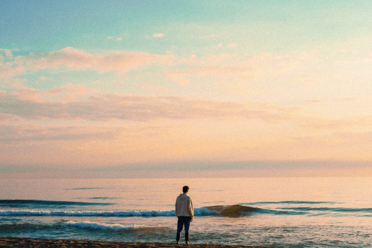 photo of a man on a beach shore at sunset looking across ocean