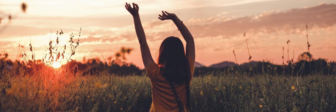 How to Cope This Summer If Your Antidepressants Make You Sensitive to Heat A woman at sunset in a peaceful field with her hand raised above her head.