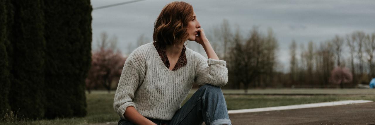 Learning to Survive the Highs and Lows of Bipolar Disorder A young white woman with red hair sitting outside looking off into the distance contemplatively