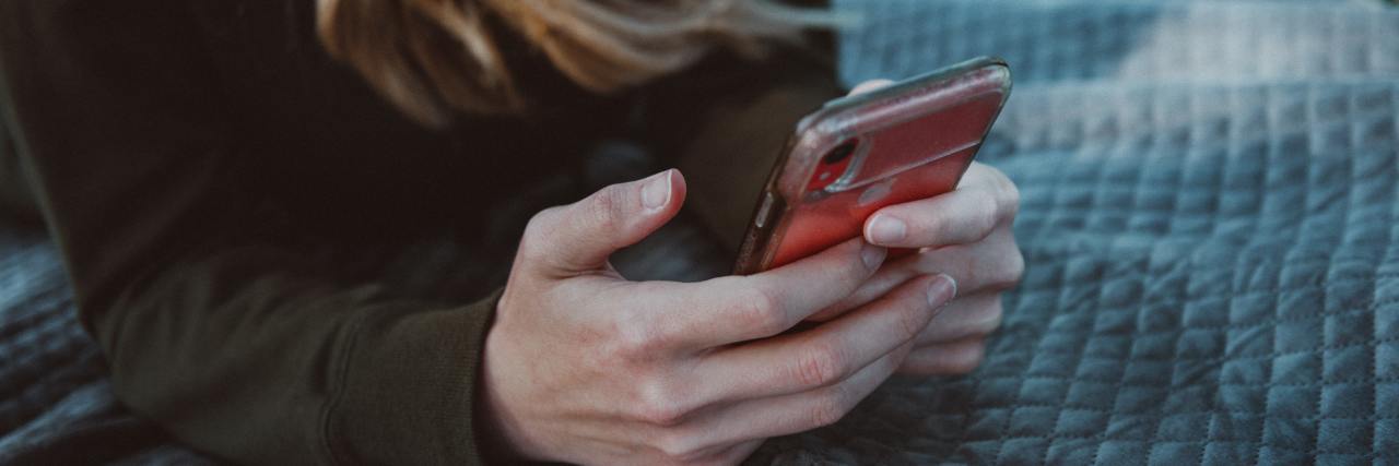 Texts Messages That Help When Someone Wants to Self-Harm photo of a woman lying on a blanket outside with a phone in her hands