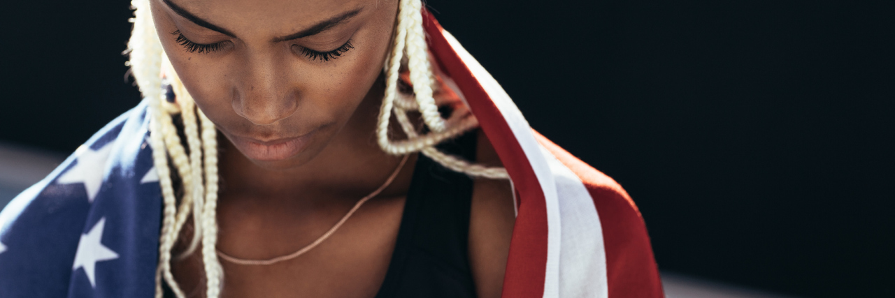 What Independence Day Means to Me As a Black Woman Living With Racial Trauma photo of a Black woman wrapped in an American flag, looking down