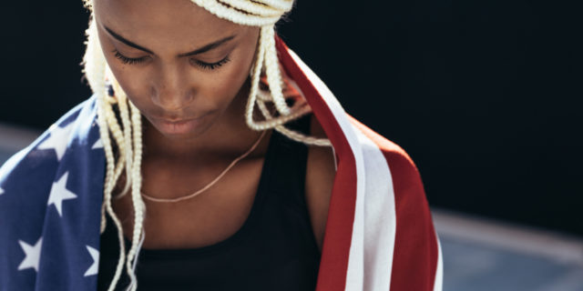 photo of a Black woman wrapped in an American flag, looking down