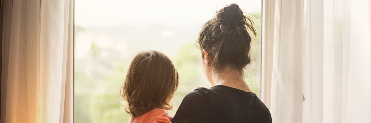 3 Stress Relief Tips for Parents of Kids With Disabilities A mother looking out the window with her young child in her arms