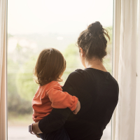 A mother looking out the window with her young child in her arms
