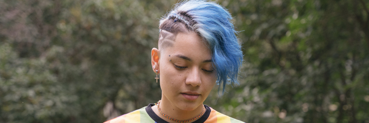 True Stories Revealing the Impact of LGBTQIA+ Status on Mental Heal Teen with short blue hair wearing a gay flag shirt