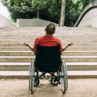 Man in wheelchair outraged in front of stairs.