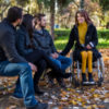 Disabled young woman in a wheelchair enjoying a autumn sunny day with friends in the park.