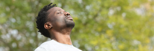 Black man breathing in fresh air outside with his eyes closed and face tilted upwards