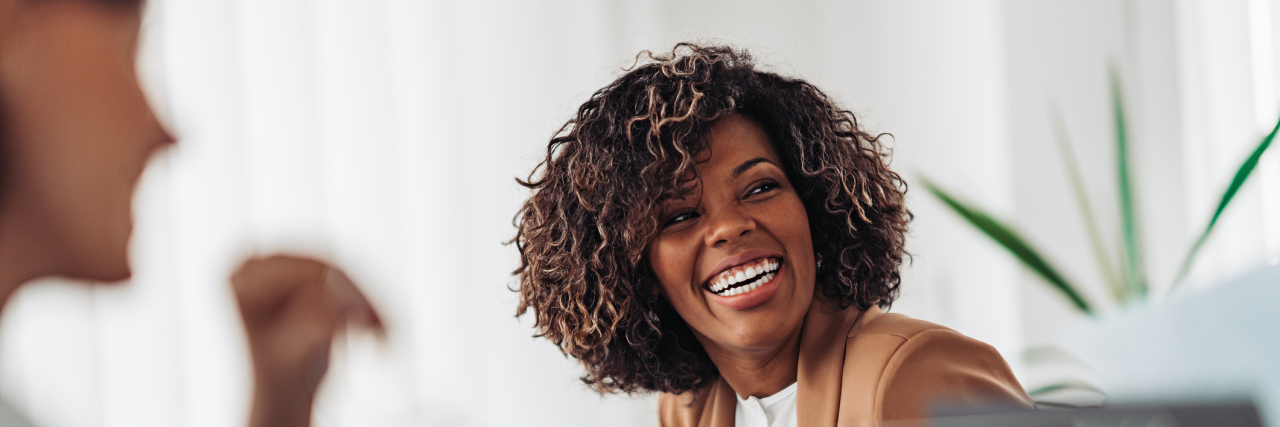 A Black woman laughing in an office meeting