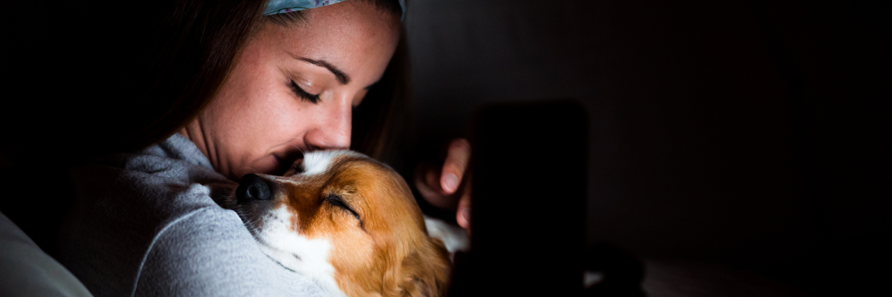 Managing the Isolation of Chronic Illness Woman cuddling with her dog on the couch.