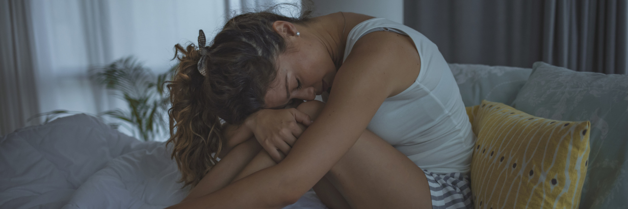 How to Cope With Nightmares After Sexual Violence Young woman sitting on a bed with her head in her knees, upset