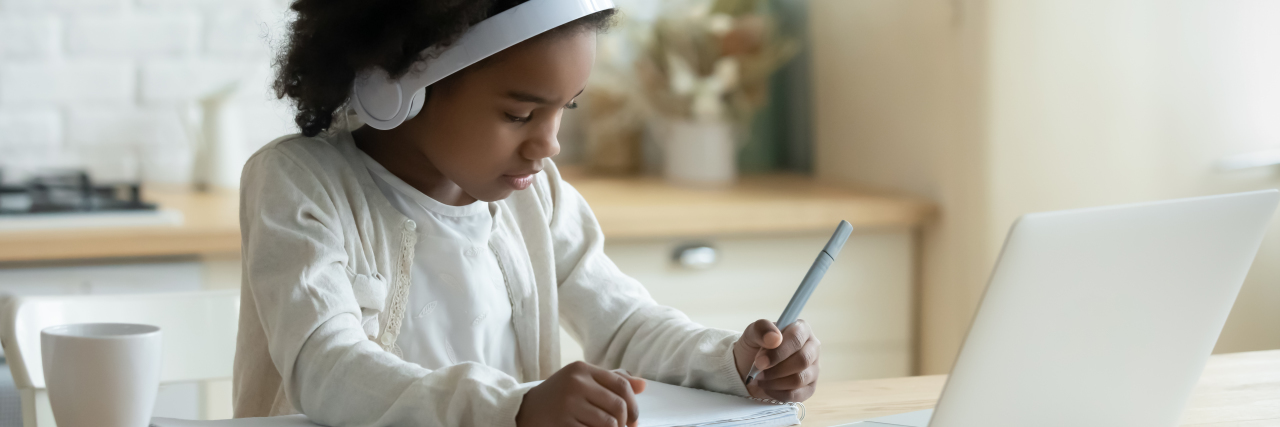 A young Black girl writing something done while participating in a virtual class