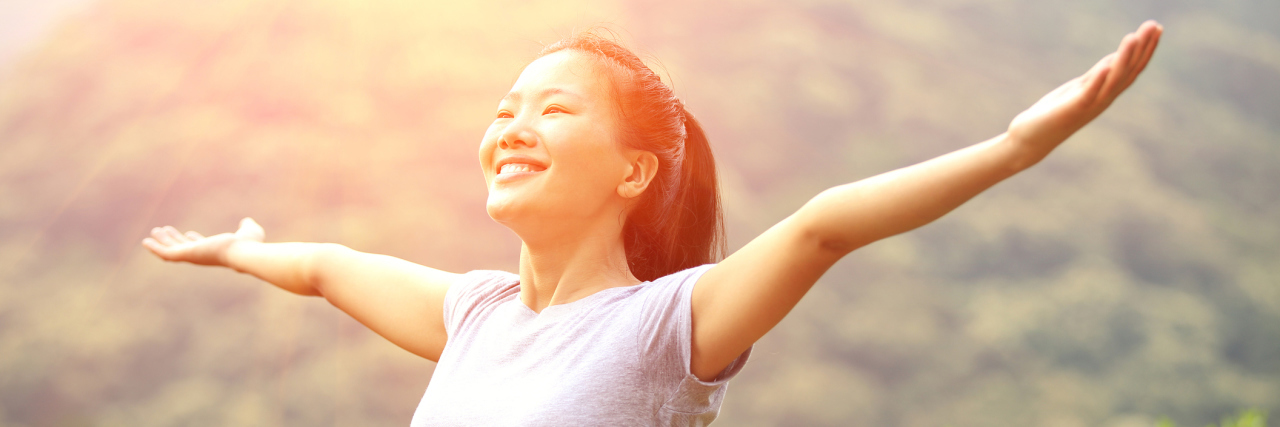 One in Four Suicide Attempt Survivors Are Now Thriving An asian woman smiling with her arms outsretched outside