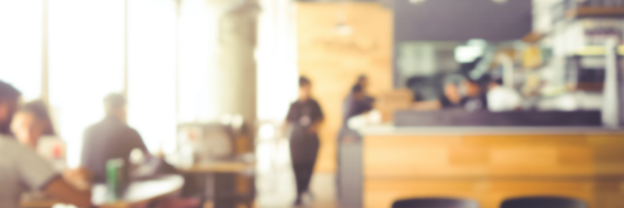 Taking Care of Myself Is 'What I Do' As Someone With Chronic Illness Wood table top with blur of people in coffee shop