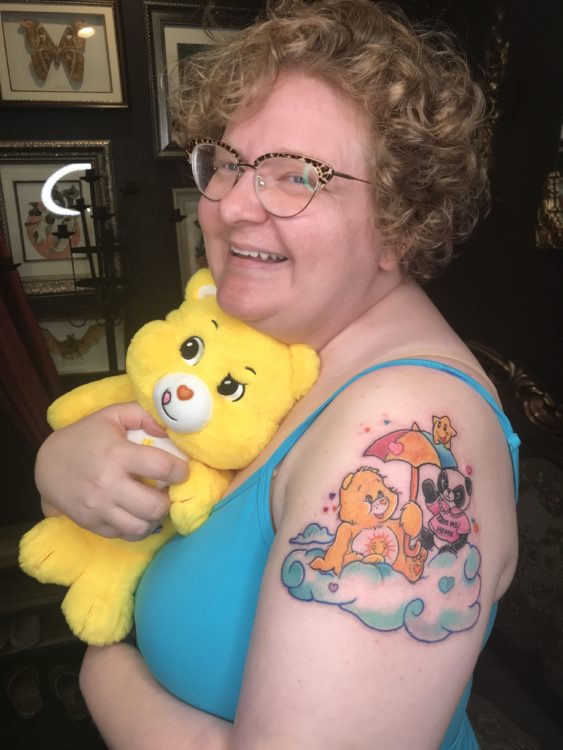 photo of the contributor with her Care Bears tattoo, while holding a Care Bear and smiling