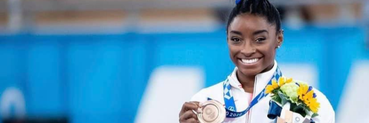 Simone Biles holding a bronze Olympic medal and flowers, smiling