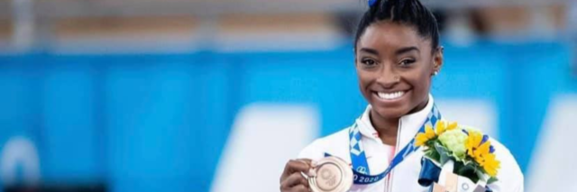Simone Biles holding a bronze Olympic medal and flowers, smiling