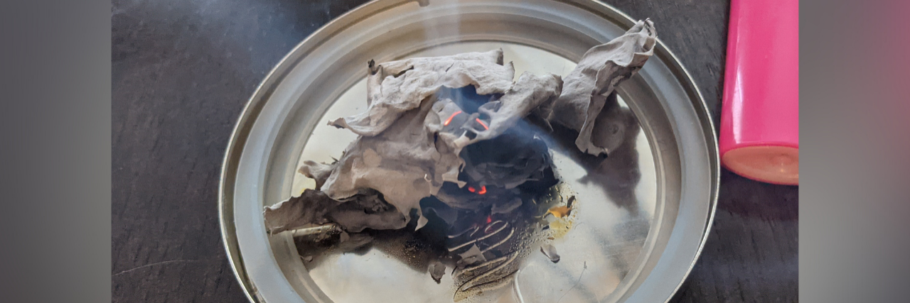 Burning My Suicide Note Made Me Feel Empowered Plate on a kitchen table with burnt paper and a pink lighter next to it