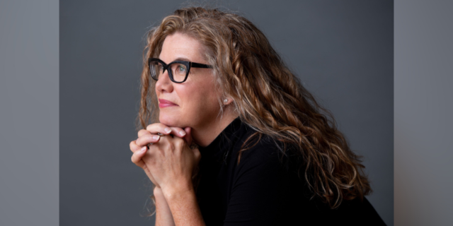 Headshot of author: middle-aged white woman with long blonde hair and glasses looking away from the camera