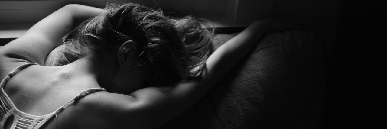 Read This If You Can't See Past Your Mental and Physical Pain Black-and-white photo of a young woman with her arms stretched across the couch, face down in pain