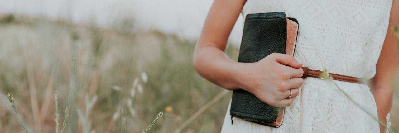 3 Reminders If You're Facing Mental Health Discrimination at Church Young woman in a white dress standing in a field holding a leather Bible at her side