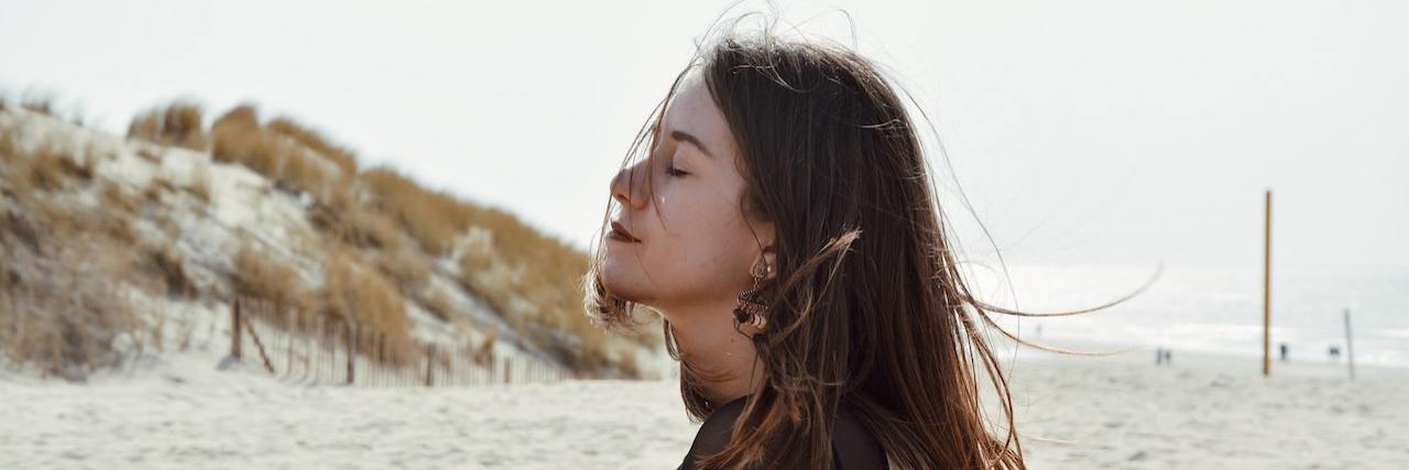 Dealing With Grief and the Loneliest Years of My Life Woman sitting on beach with eyes closed, arms wrapped around herself