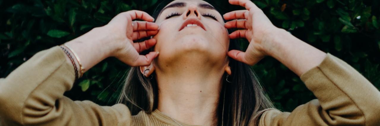 Read This If You're Terrified of Becoming Suicidal Again photo of a woman with her head raised and hands to her head, looking upset