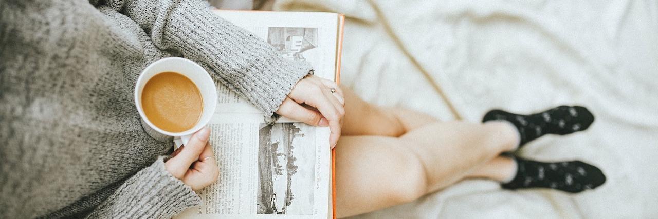 Effective Ways to Reduce Anxiety Photo of woman wearing a sweater, holding a book and cup of coffee while relaxing at home