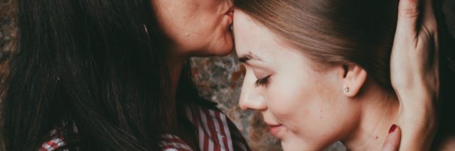 photo of a mother kissing her young adult daughter on the forehead