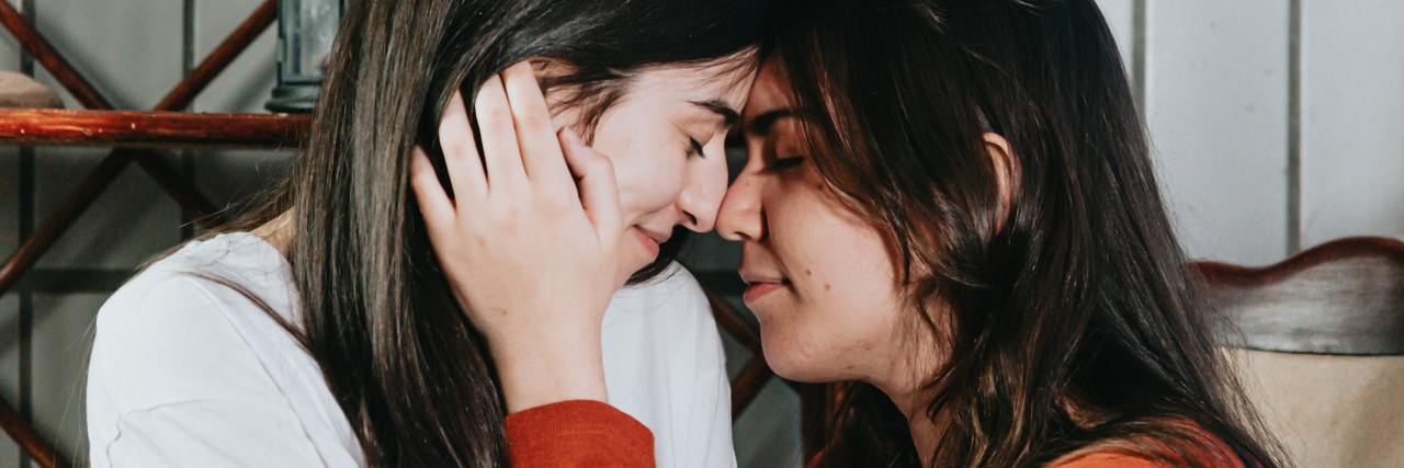 How Alyson Stoner's Religious Shame Resonated With Me as a Bisexual photo of two women with their foreheads resting against each other's and their eyes closed, one with her hand against the other's cheek