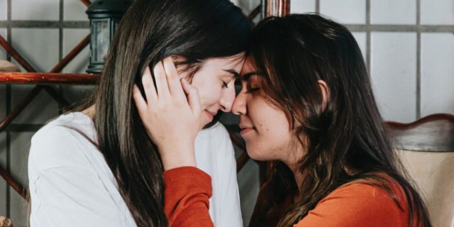 How Alyson Stoner's Religious Shame Resonated With Me as a Bisexual photo of two women with their foreheads resting against each other's and their eyes closed, one with her hand against the other's cheek