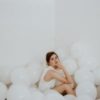 Photo of woman in white room sitting on the floor among white balloons