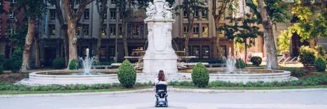 Woman wheelchair user looking at statue in park.