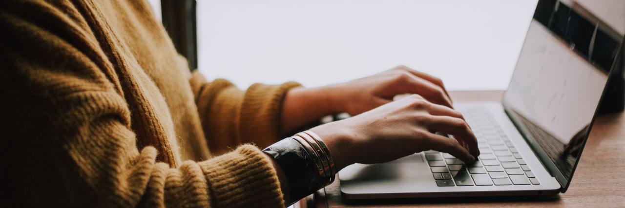 Why Looking Your Therapist Up Online Is Important A woman in a thick yellow sweater typing on a laptop, side profile, bottom-half shot only