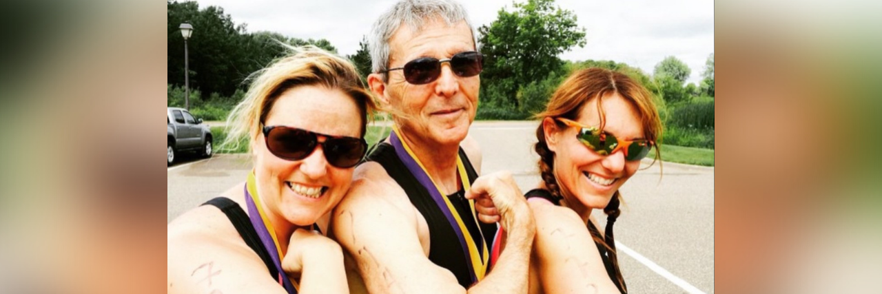 What It's Like Being a Caregiver to My Father With Alzheimer's Photo of contributor, her father and her sister making a muscle before starting a triathlon