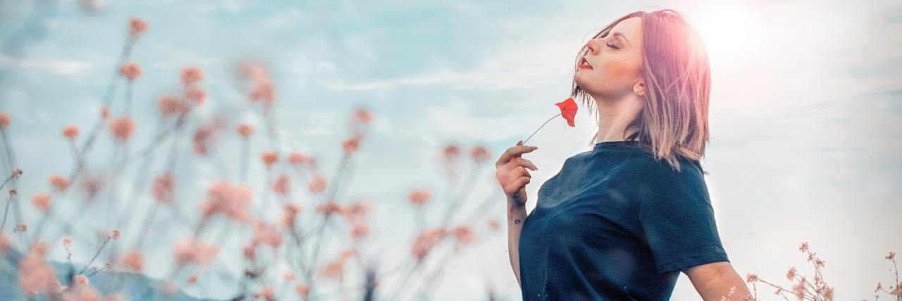 You Have Unconditional Worth Regardless of Physical and Mental Illness photo of a woman in a field holding a flower, her eyes closed and smiling with happiness