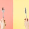 Photo of person's hands holding a knife and fork, on peach and yellow background