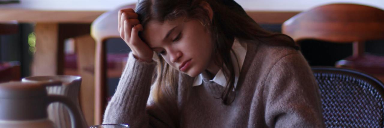 photo of a young woman sitting in a cafe looking sad