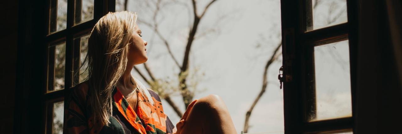 Why Healing Mental Health Is Like Healing a Broken Bone photo of a woman sitting on a windowstill in sunlight with trees behind her