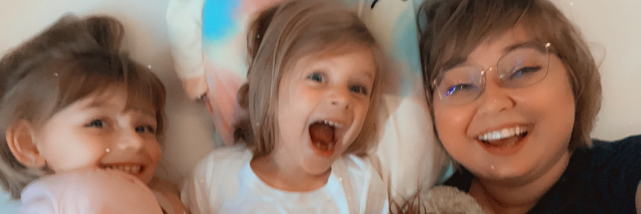 Explaining My Chronic Illness and Immunodeficiency to a Child Photo of contributor laying next to two young nieces all smiling at the camera