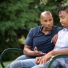 Black man talking to his son, sitting on a park bench