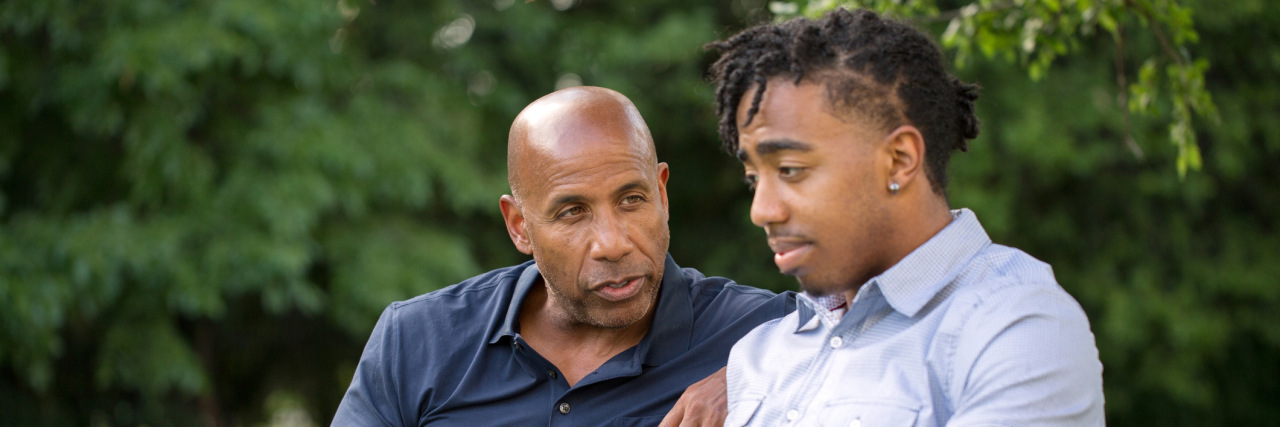 Black man talking to his son, sitting on a park bench