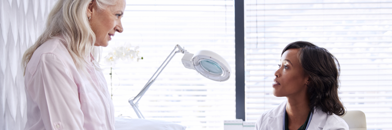 What 100 Doctor Appointments in One Year Have Taught Me Mature Woman In Consultation With Female Doctor Sitting On Examination Table In Office