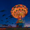 Carousel lit up at night with bright colors and silhouettes of people swinging rapidly around