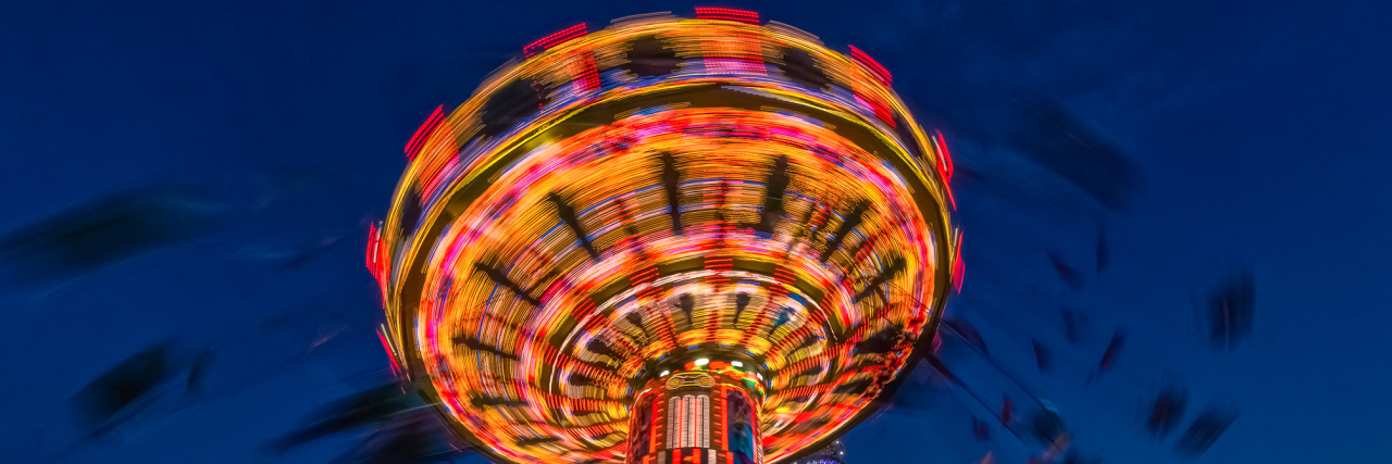 Carousel lit up at night with bright colors and silhouettes of people swinging rapidly around
