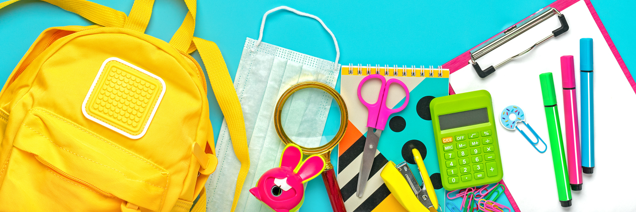 Back to school. Yellow backpack with school supplies, protective medical mask, calculator, scissors.